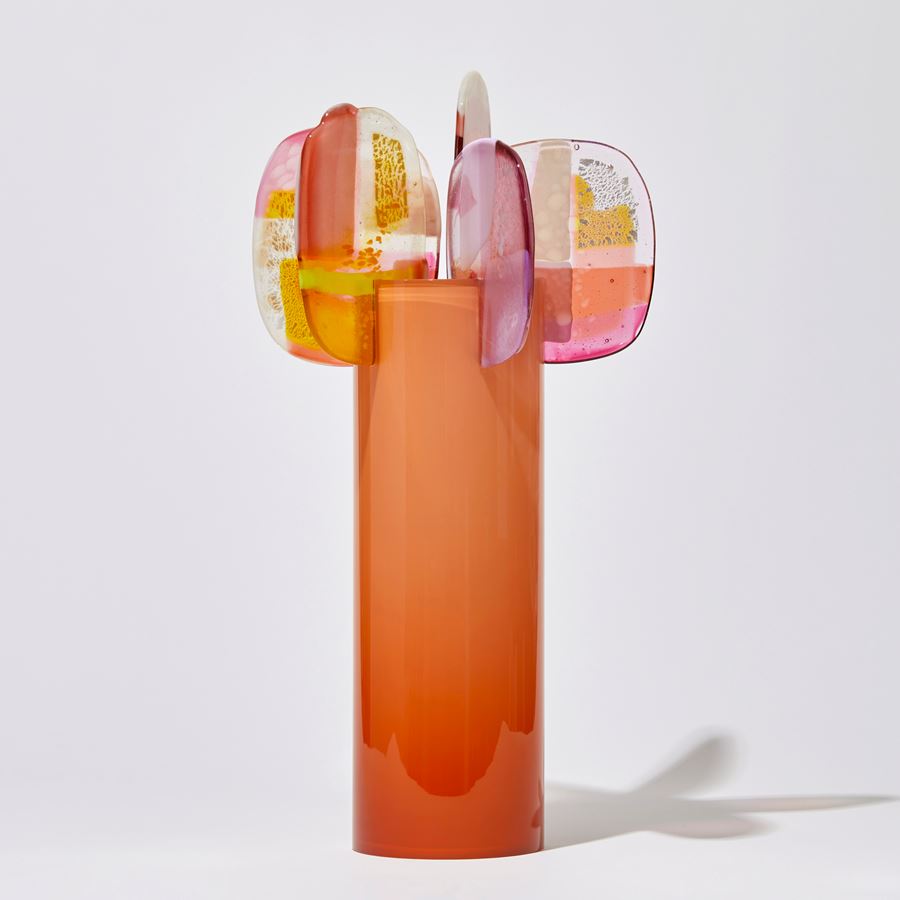 opaque peachy orange cylinder with colour fade from top to bottom and five rounded petals overlapping and perched on the top rim with abstract patterns in pink peach orange yellow white and clear handmade from blown and fused glass